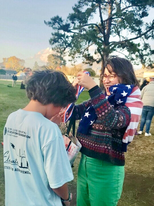 Marisa Gomez putting a medal over her son's head at a school field